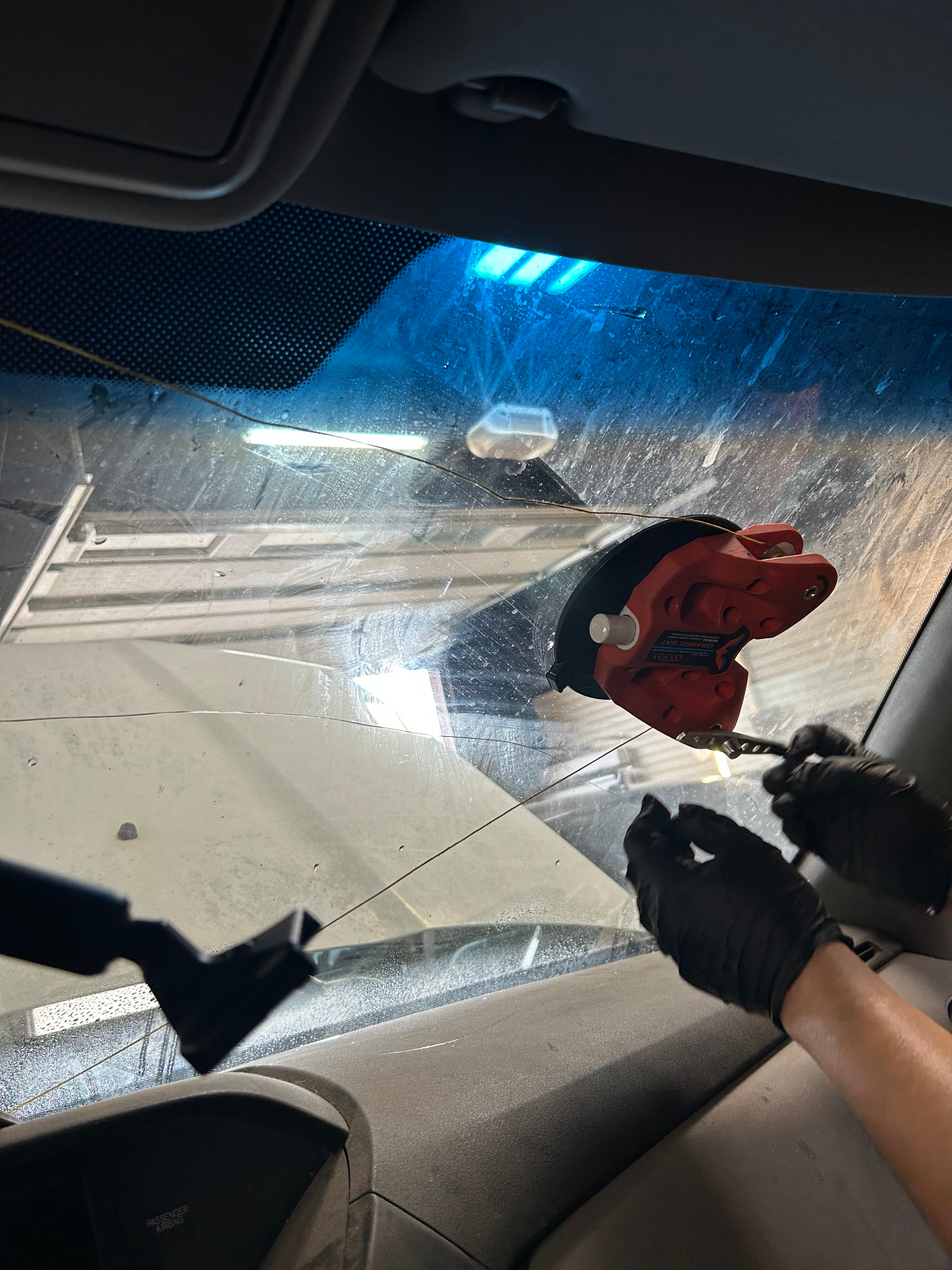 Technician removing damaged windshield using cut wire tool